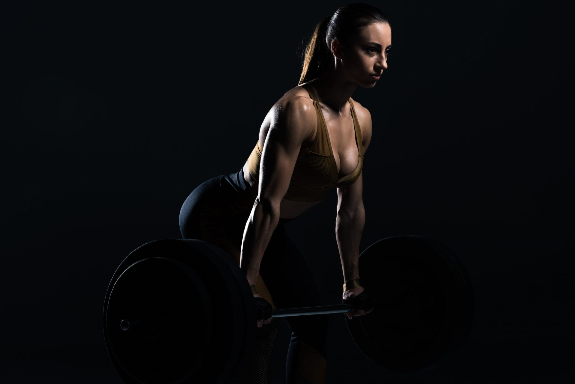 beautiful female bodybuilder lifting barbell, isolated on black
