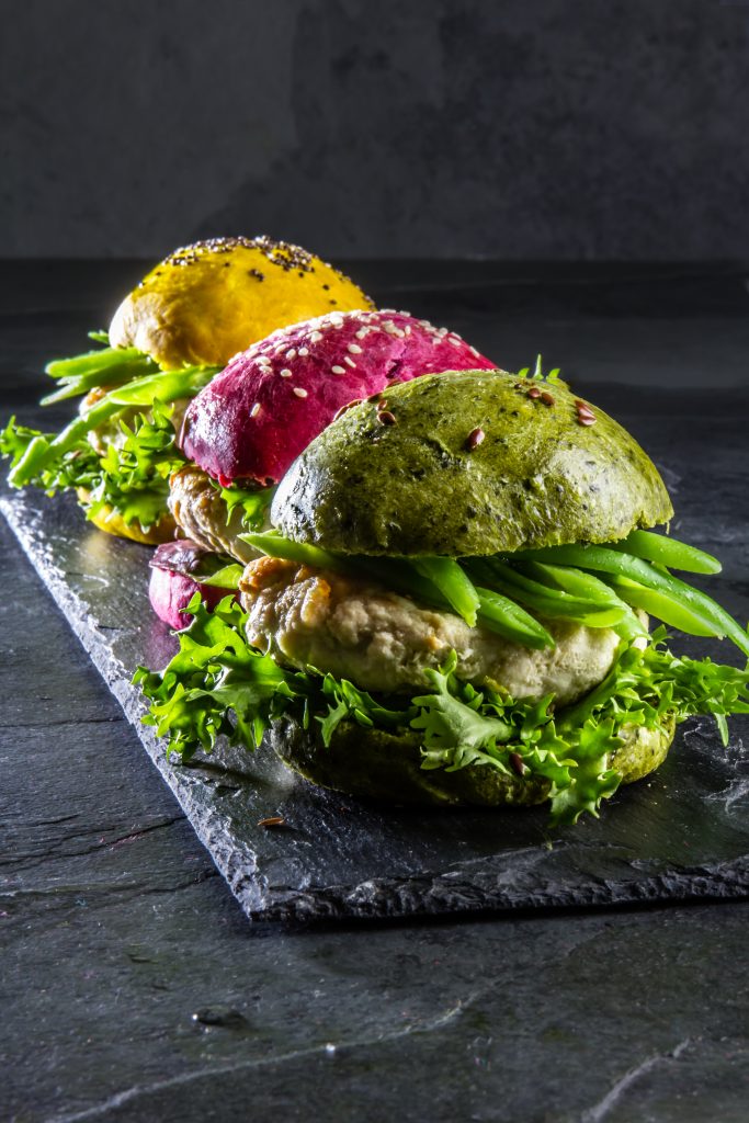 Colored green, yellow and purple burgers on slate board, slate background