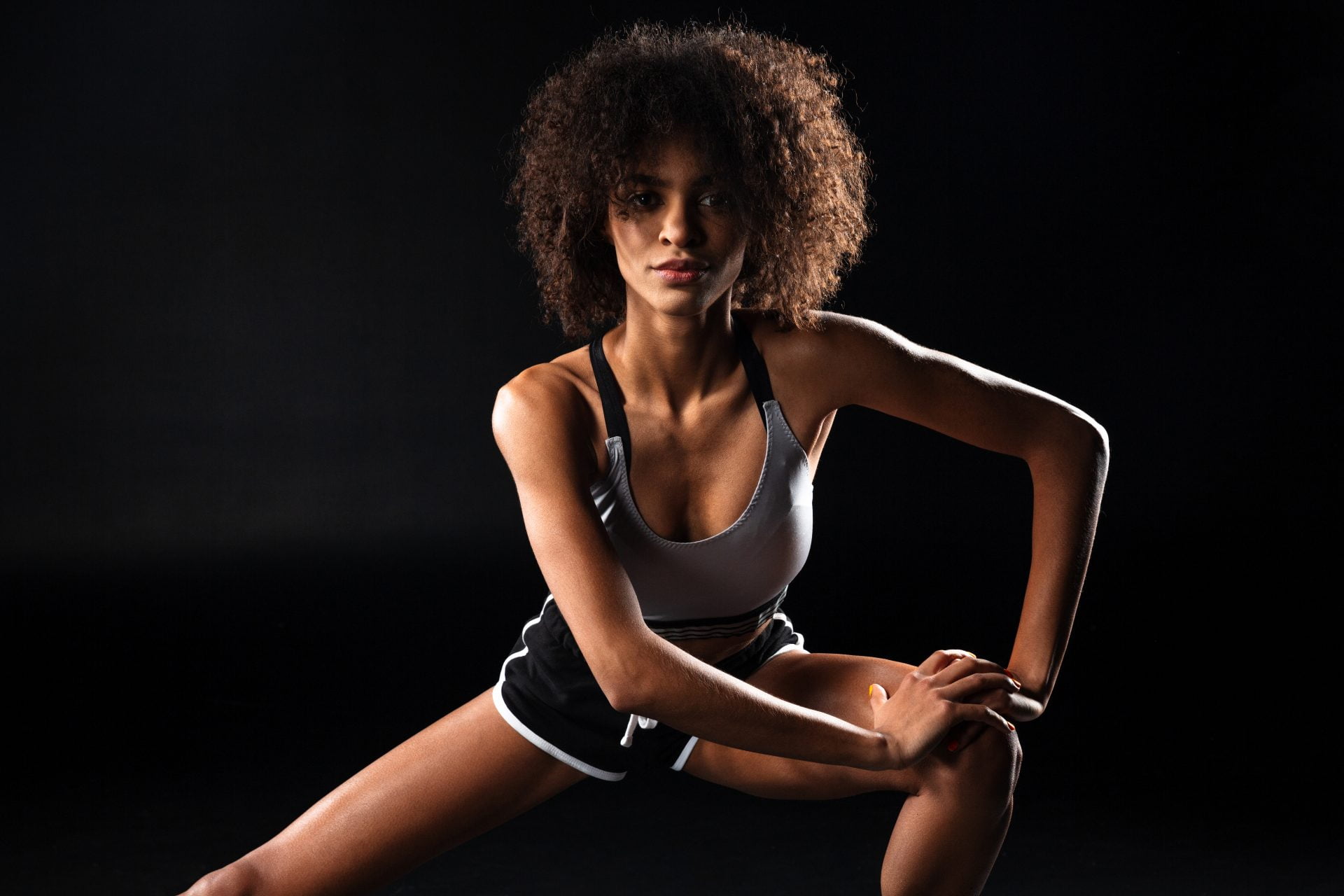 Image of focused african american sportswoman stretching her leg