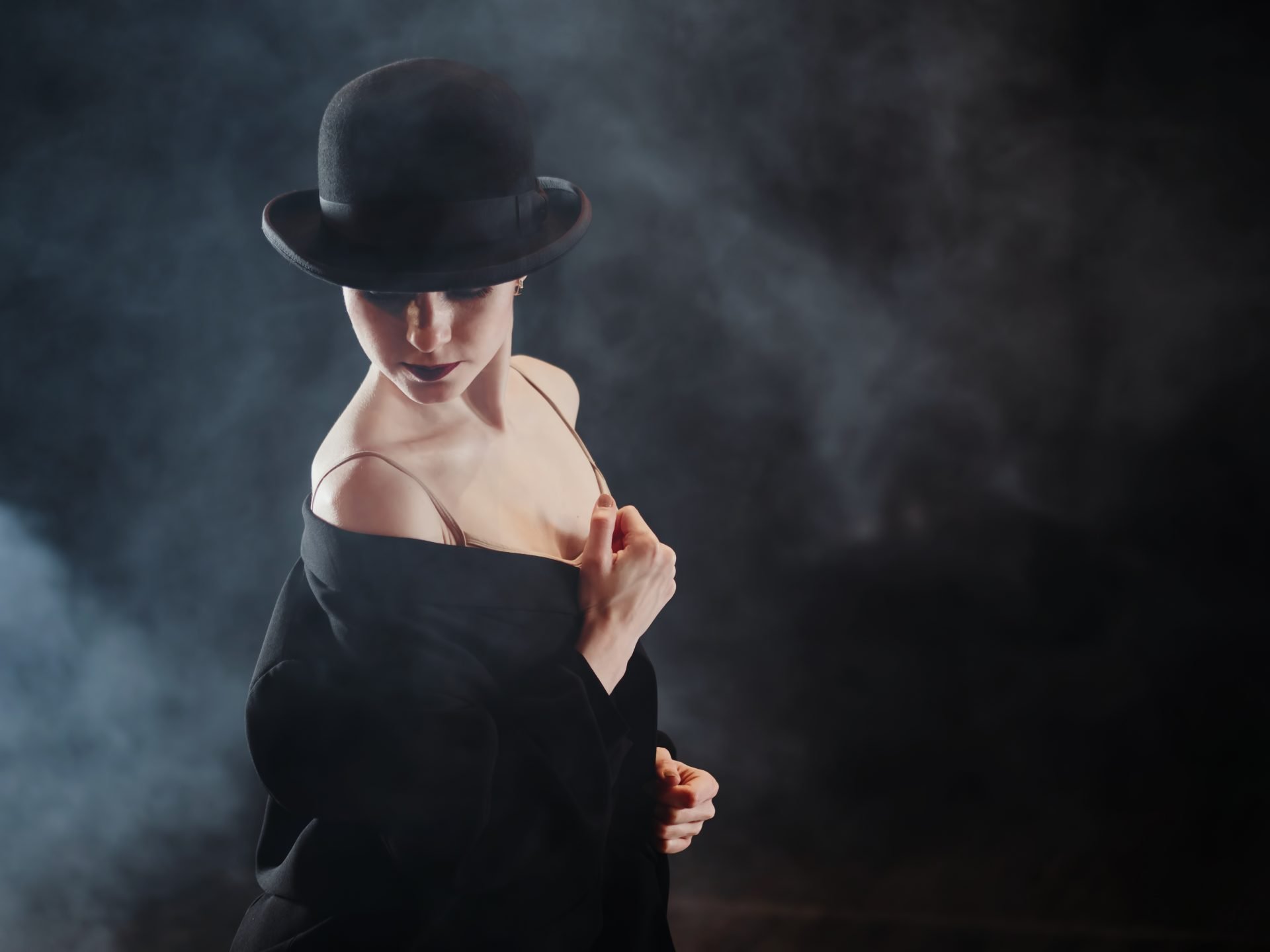 Woman in black costume on scene. Young beautiful ballerina on smoke stage dancing modern ballet. performs smooth movements with hands against spotlights background.